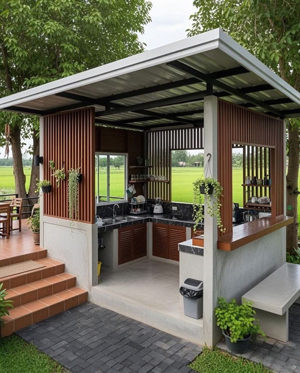 A modern outdoor kitchen structure with wooden slats, concrete counters, and a metal roof near green fields.
