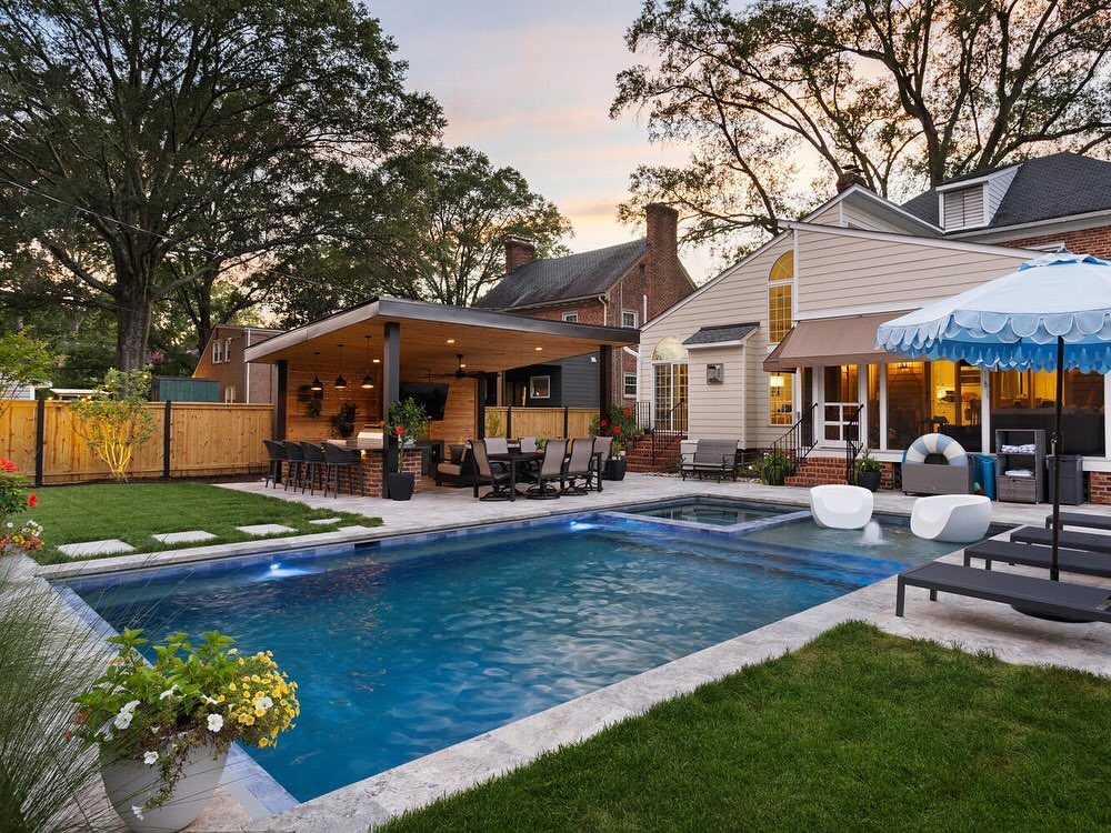 A luxury backyard with a swimming pool, stone patio, and a covered outdoor bar and kitchen pavilion.