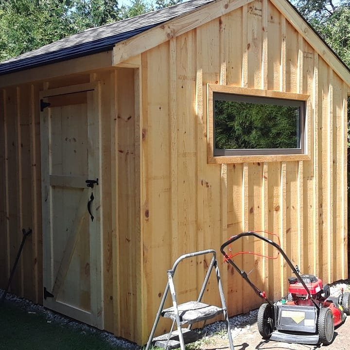 A wooden garden shed featuring vertical board and batten siding and a small window.