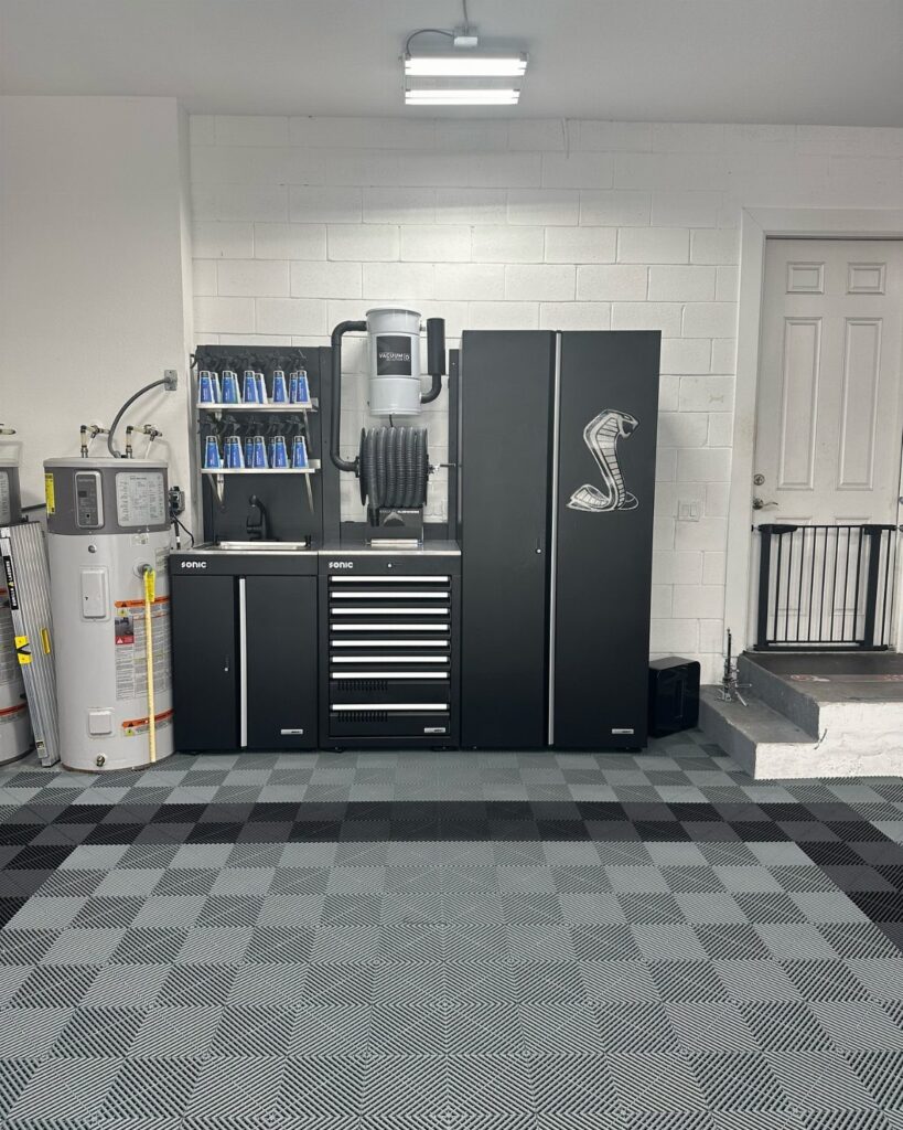 Black tool cabinets and organized supplies arranged on a patterned grey garage floor.