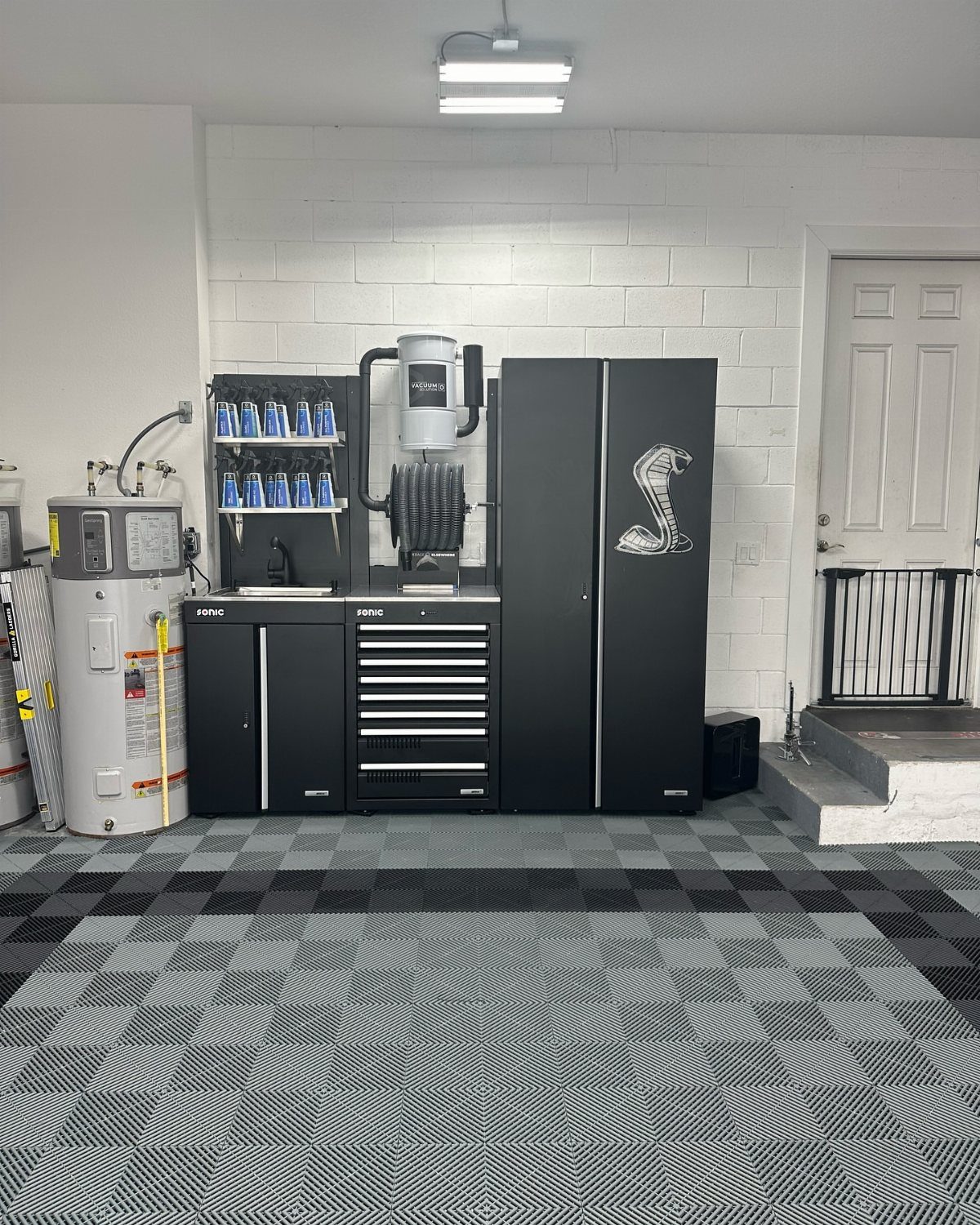 Black tool cabinets and organized supplies arranged on a patterned grey garage floor.