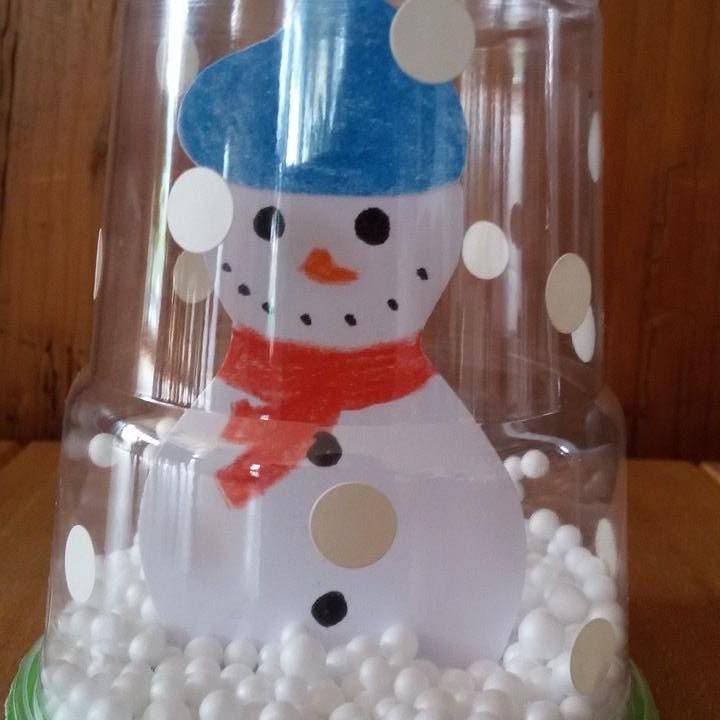 A snowman paper cutout craft inside a clear plastic bottle filled with white foam snow.