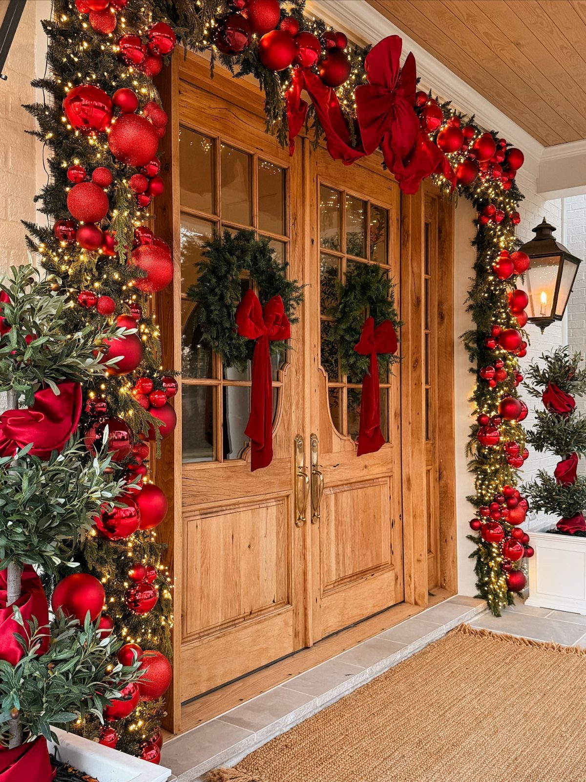 Wooden double doors decorated with festive evergreen garlands, red ornaments, and large red bows.