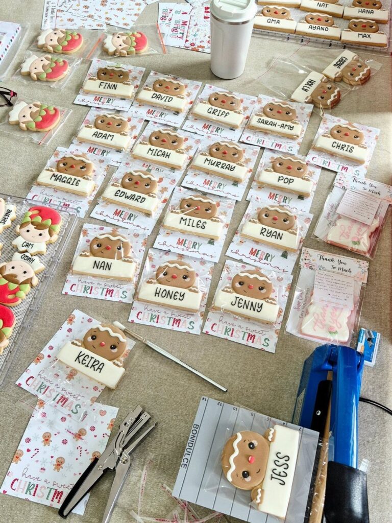 Decorated gingerbread man cookies with names written on icing, laid out on a table with crafting supplies.