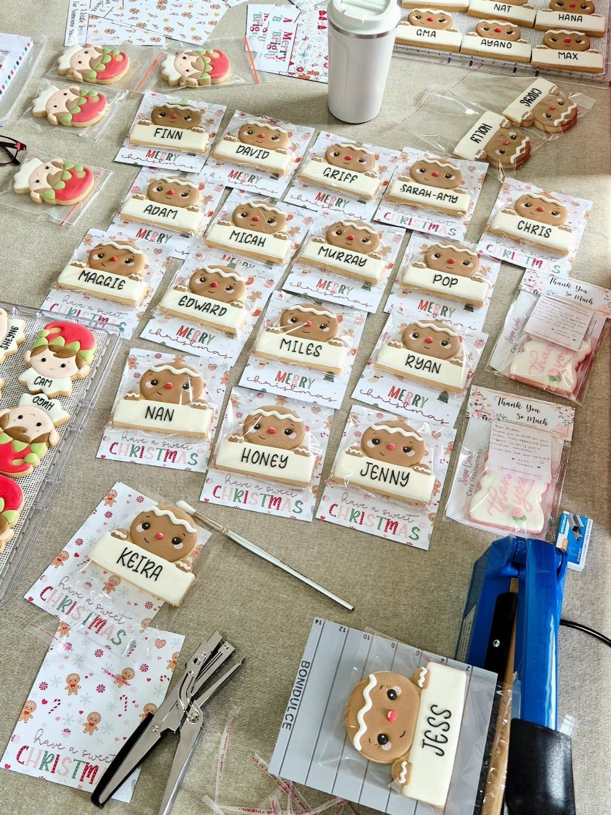 Decorated gingerbread man cookies with names written on icing, laid out on a table with crafting supplies.