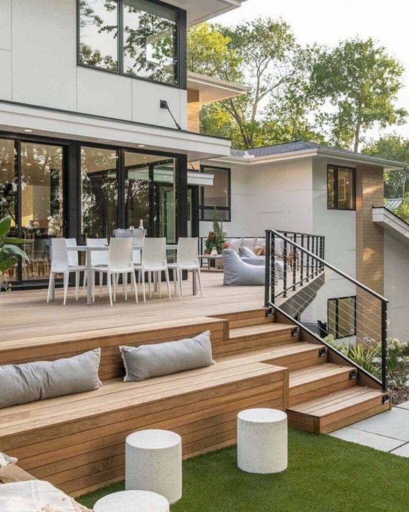 A modern multi-level wooden deck with built-in seating, dining area, and contemporary house architecture.
