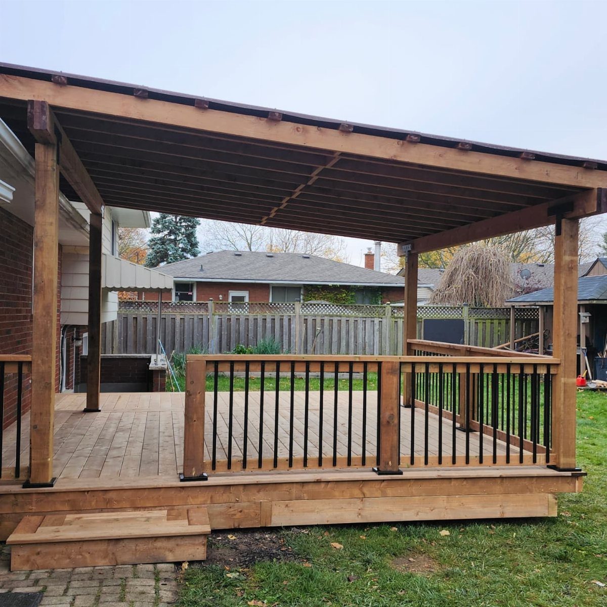 A wooden outdoor deck with a large attached roof and black metal railing spindles.