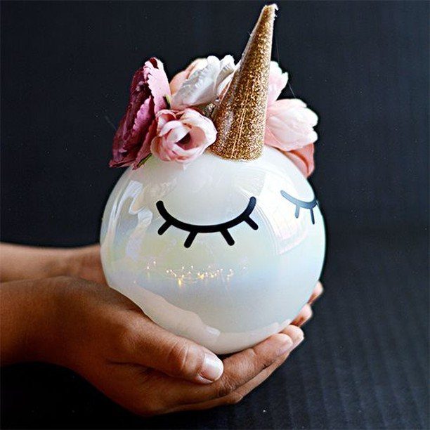 A white iridescent unicorn ornament with a gold horn and pink flowers held in hands.
