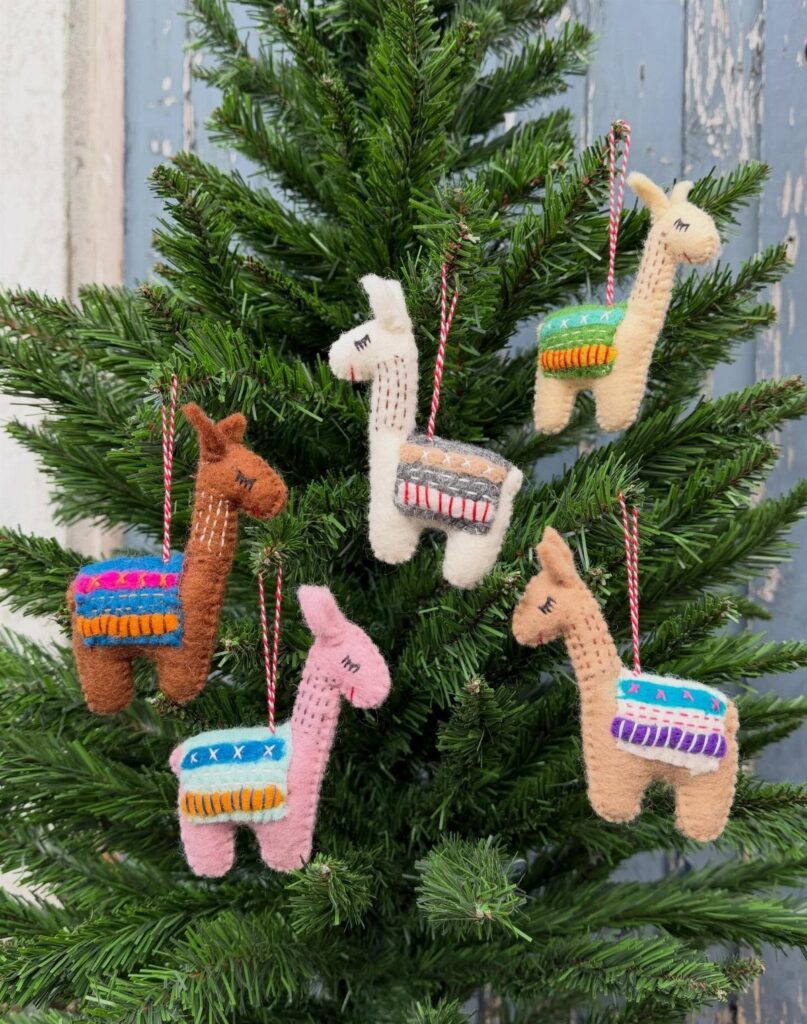 Knitted llama ornaments in different colors hanging on the branches of a green Christmas tree.