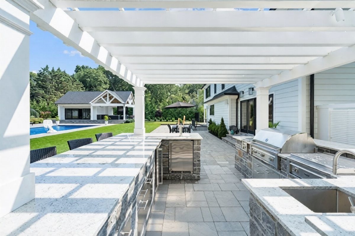 Modern outdoor kitchen with granite counters and stainless steel grill overlooking a swimming pool.