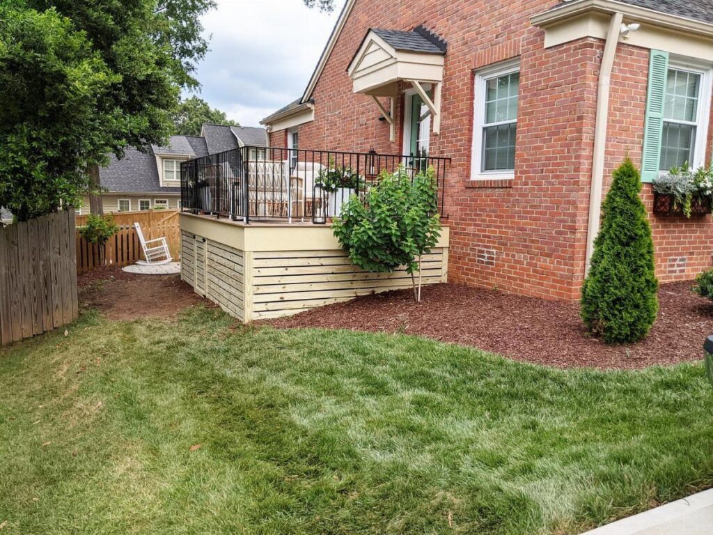 A wooden deck with horizontal light-colored slats used as skirting against a brick house.