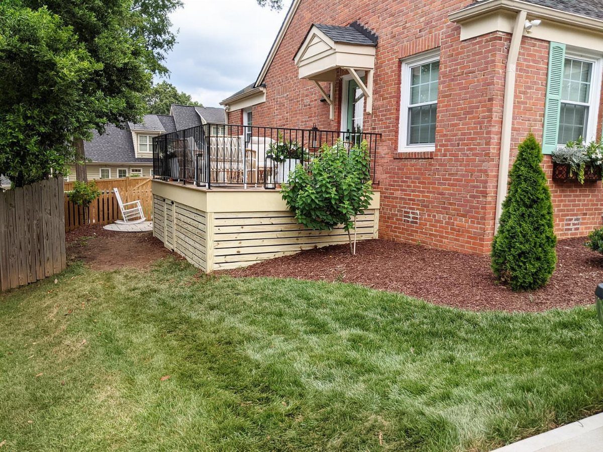 A wooden deck with horizontal light-colored slats used as skirting against a brick house.