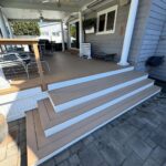 A wide, multi-level wooden deck with white trim attached to a grey house with outdoor furniture.