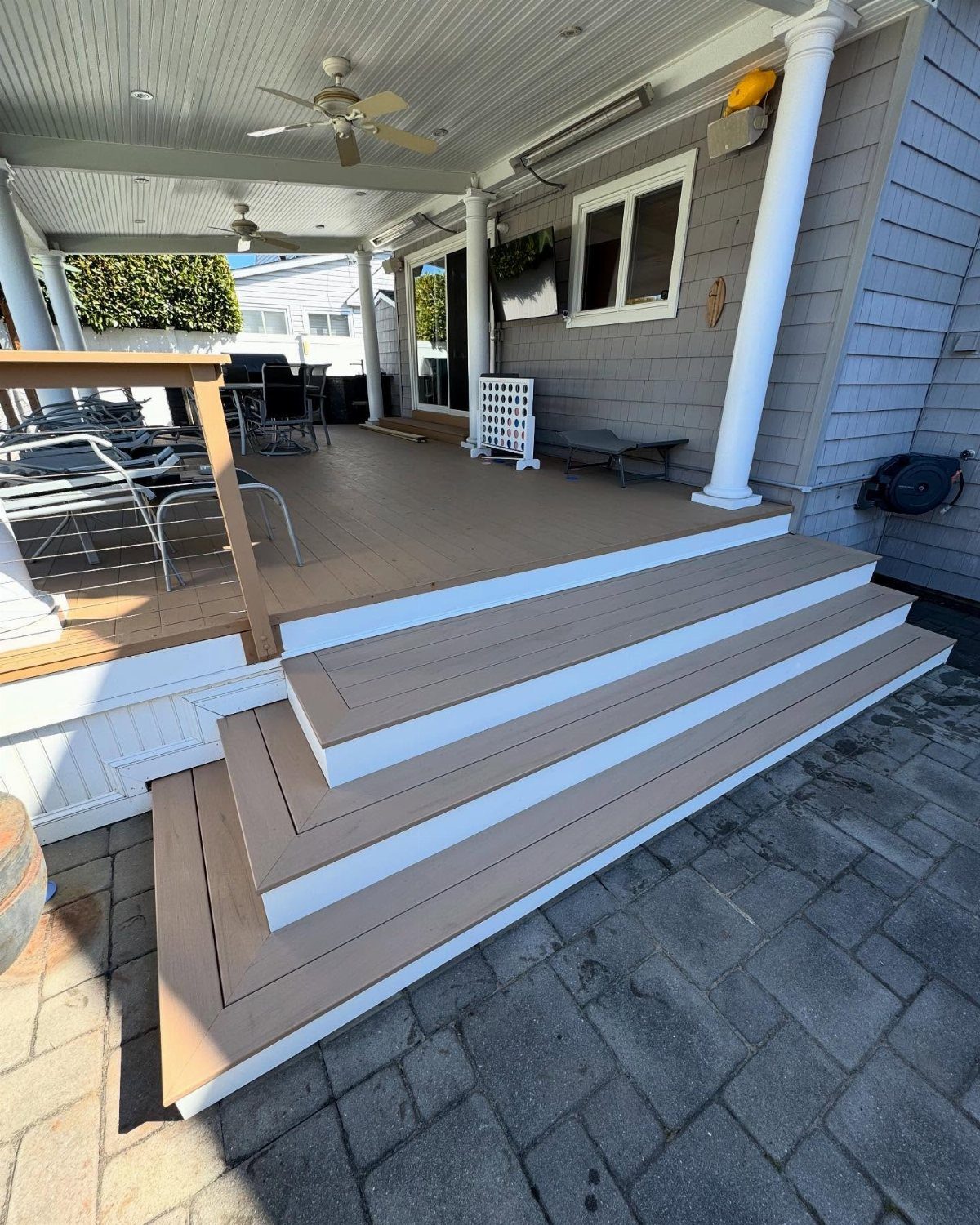 A wide, multi-level wooden deck with white trim attached to a grey house with outdoor furniture.